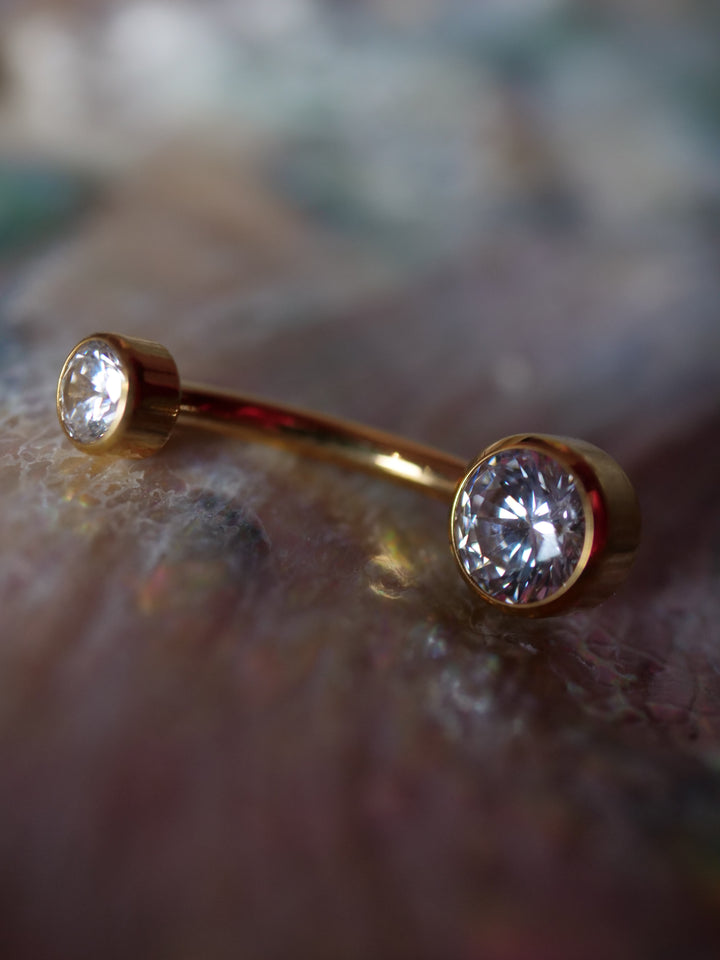 Gold belly button ring with clear gemstones on a blurred background
