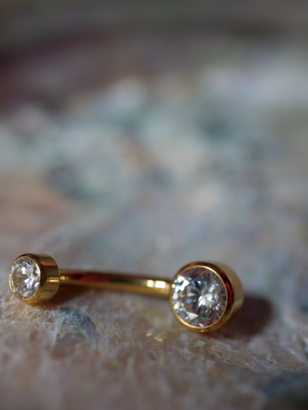 Gold belly button ring with clear gemstones on a textured surface