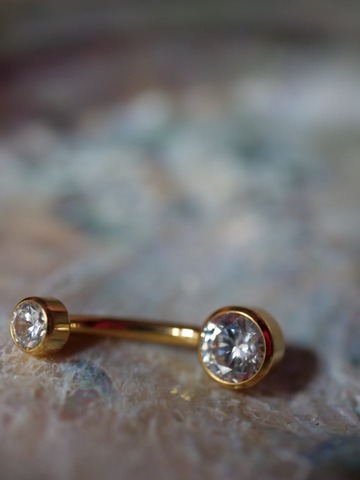 Gold belly button ring with clear gemstones on a textured surface