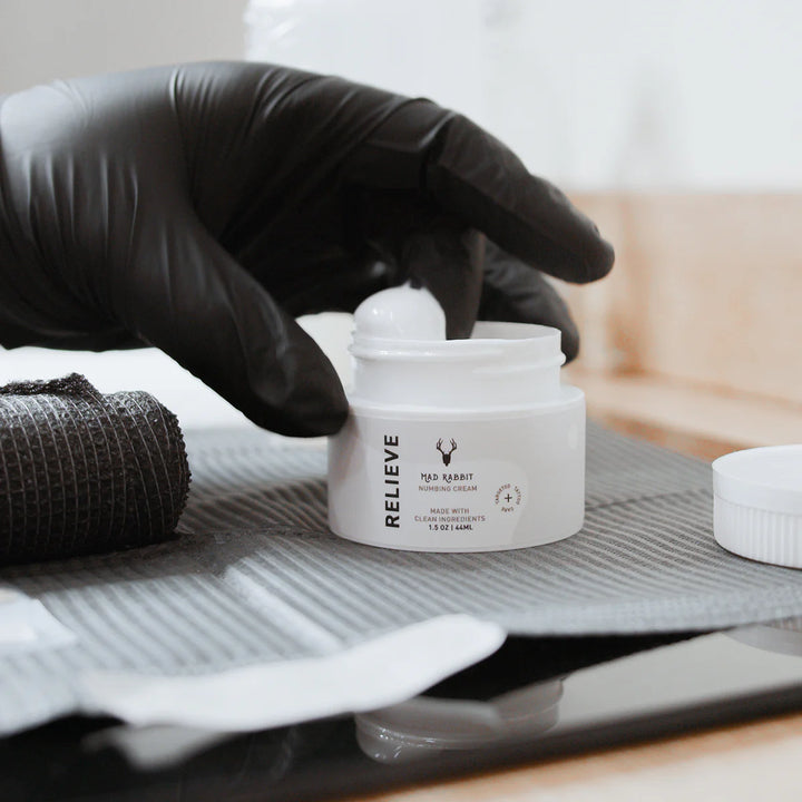 mad rabbit numbing cream on a tattoo setup with a gloved hand in the cream 
